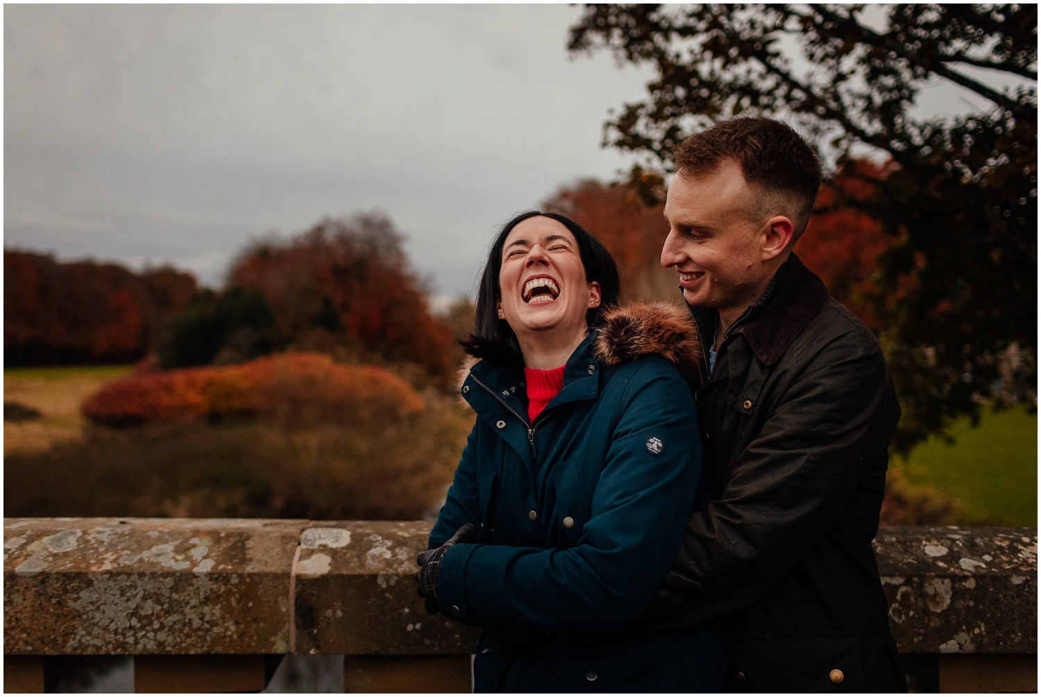 Couple in Pollok Park in Autumnstanding on bridge beside pollok house laughing couples shoot engagement shoot