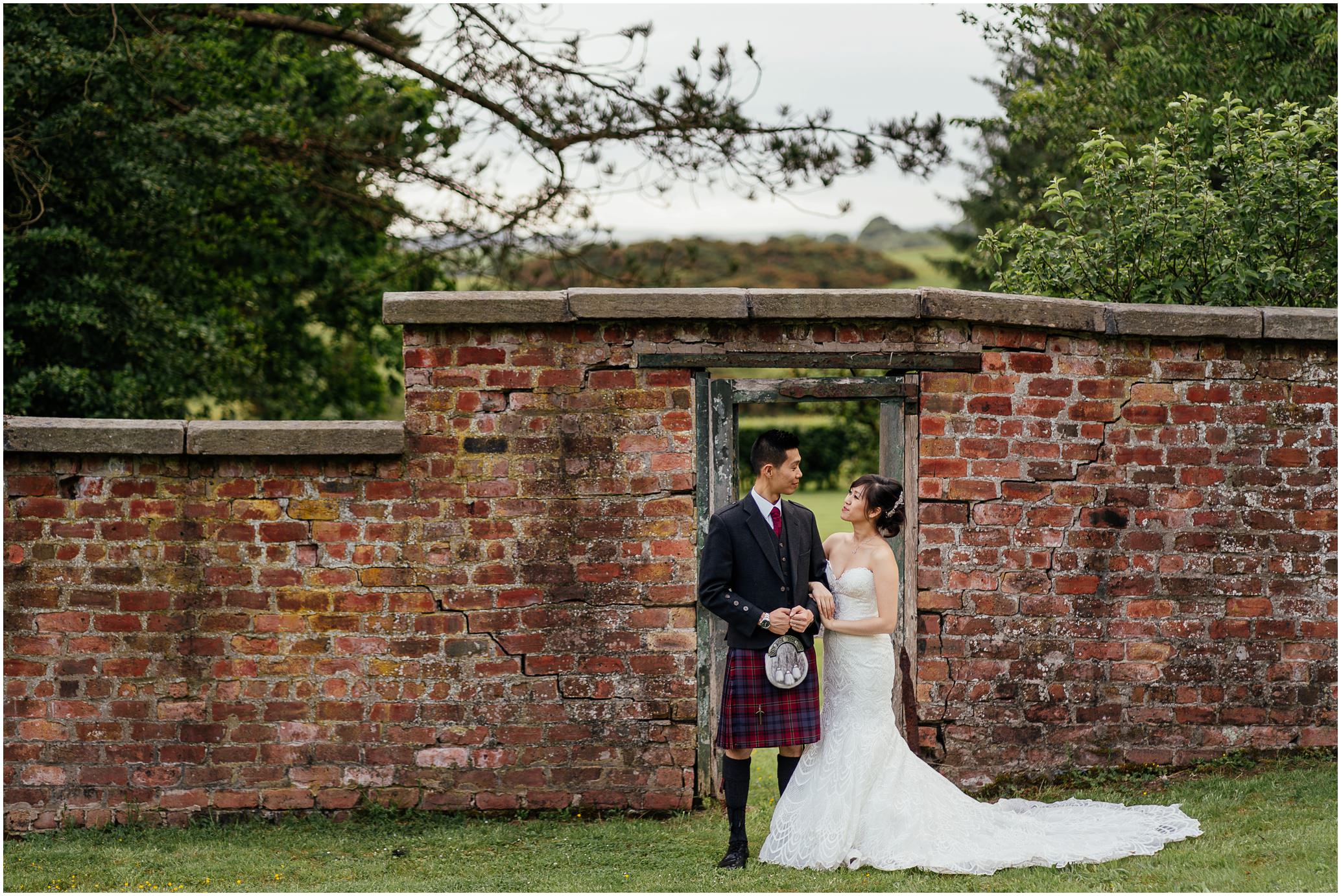 bride and groom linking arms and looking into each others eyes in walled garden with brick wall and trees behind them post wedding photoshoot glasgow fotomaki photography