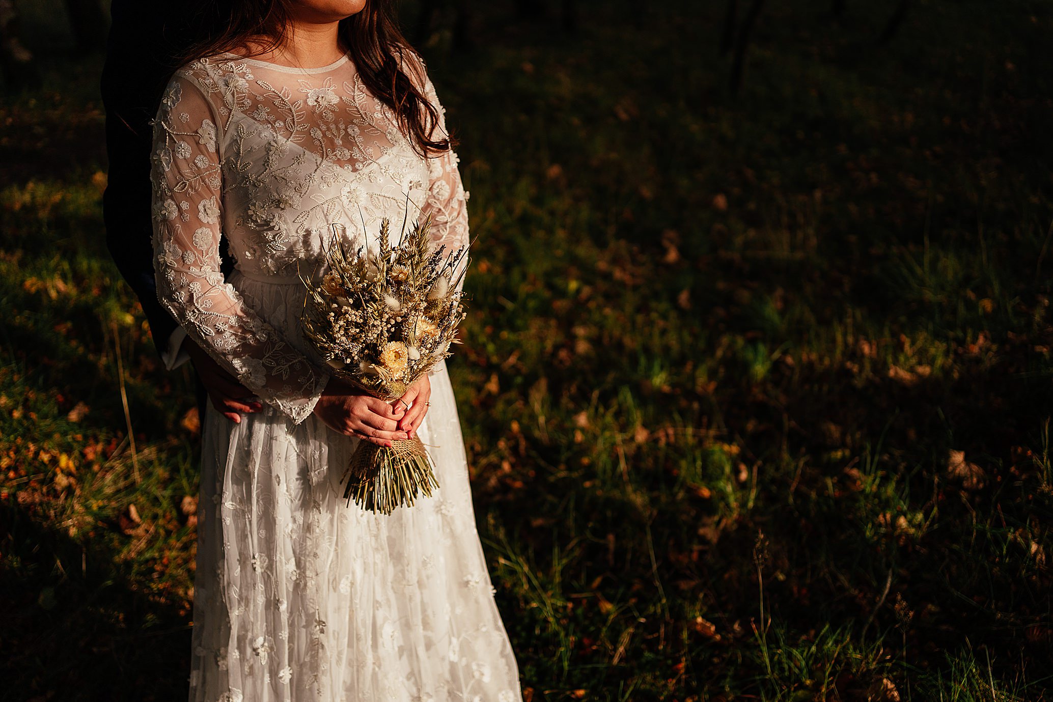 warm light from the sun shining on bride in beautiful white dress holding bridal bouquet with dark shadows over grass in background monachyle mhor wedding photoshoot fotomaki photography