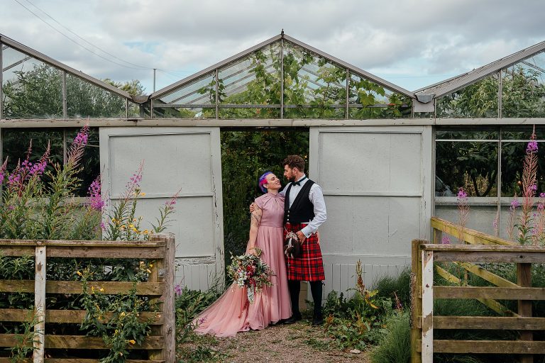 italian bride wearing pink wedding dress and belgian groom look into each others eyes as they pose in front of greenhouse outdoor wedding secret herb garden wedding