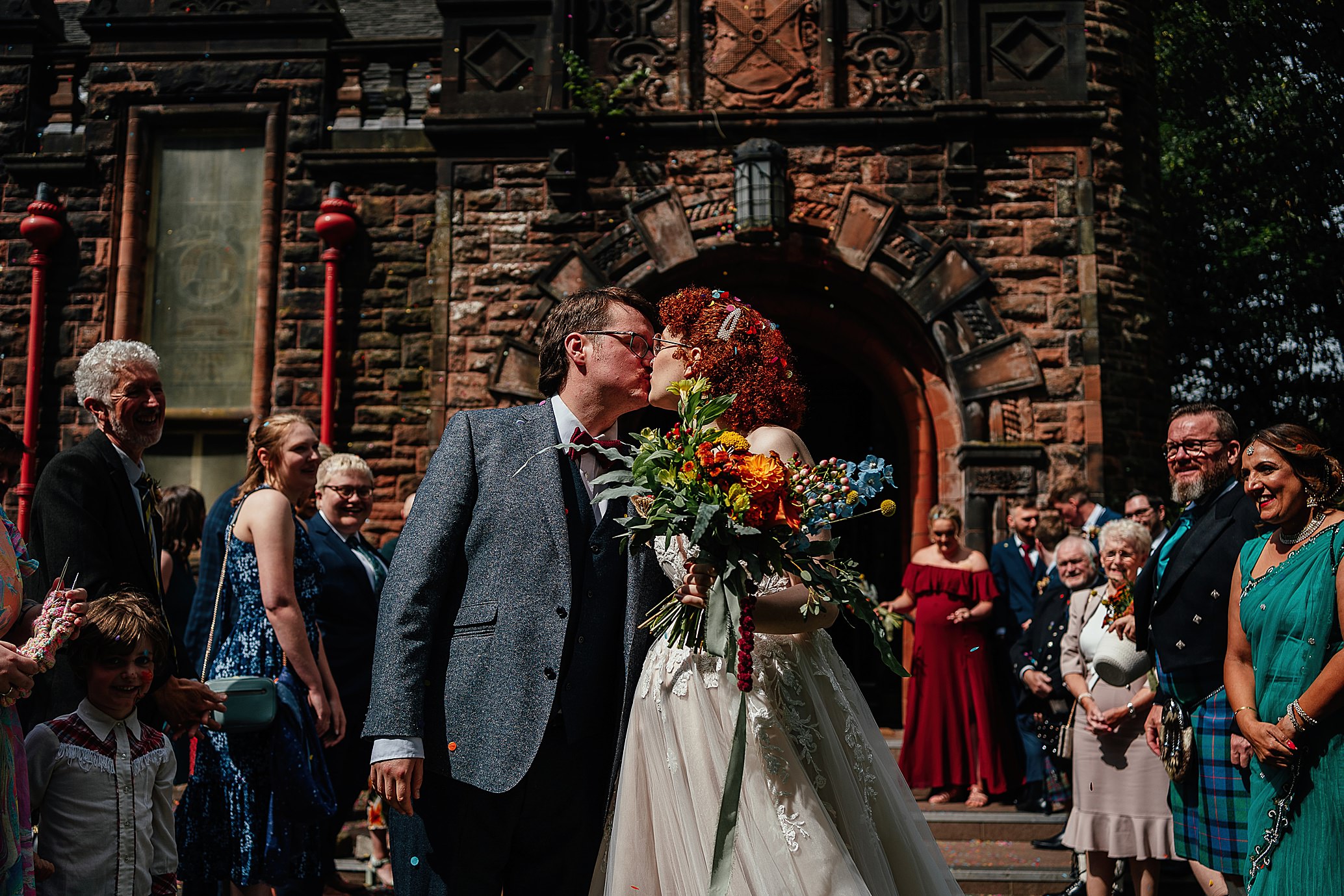 bride and groom kiss outside hall as guests look on relaxed pollokshields burgh hall wedding