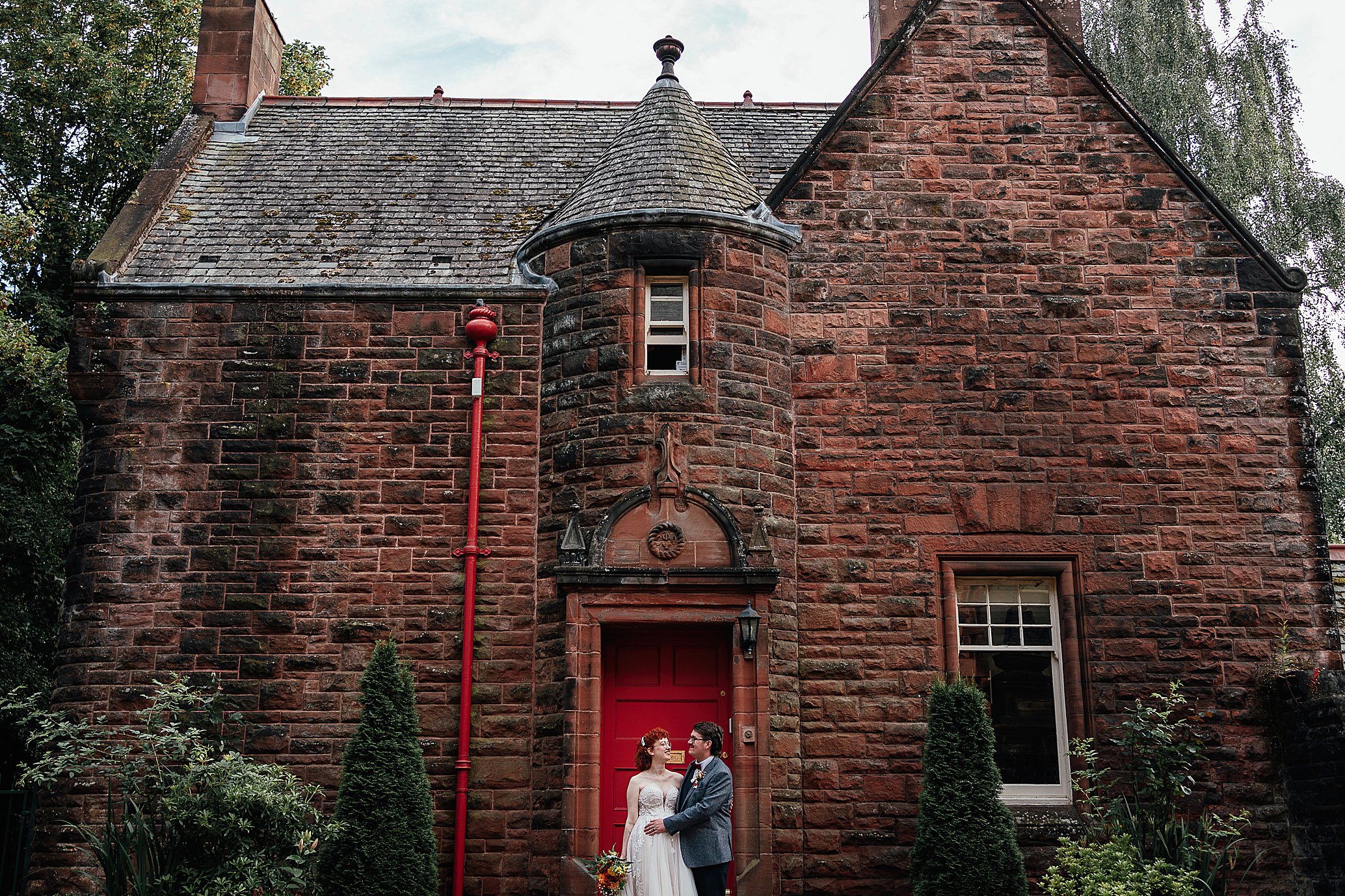 bride and groom hug in front of old red brick building natural pollokshields burgh hall wedding