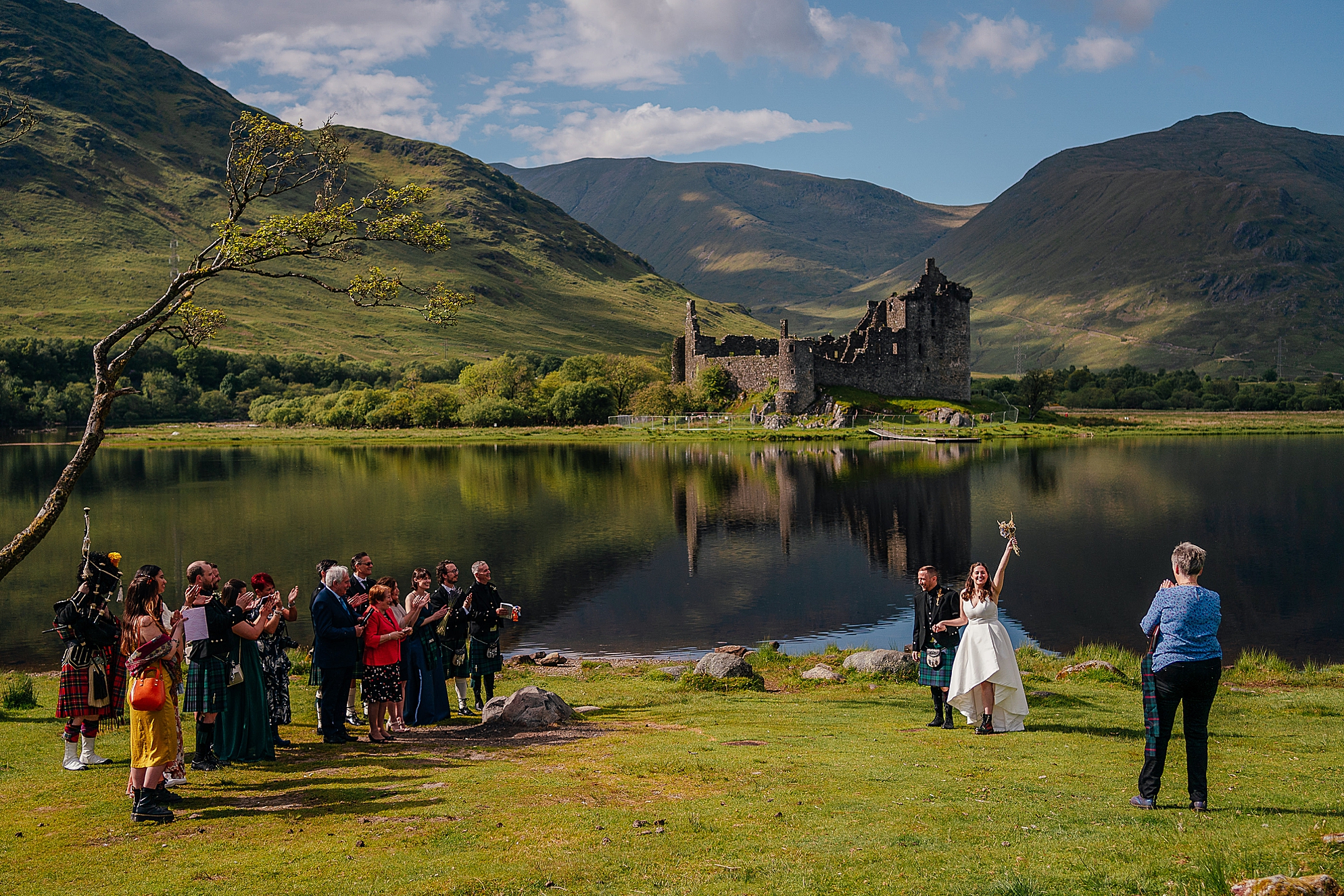 bride and groom celebrating at the end of their kilchurn castle wedding ceremony outdoors with a beautiful moody view of loch awe scotland