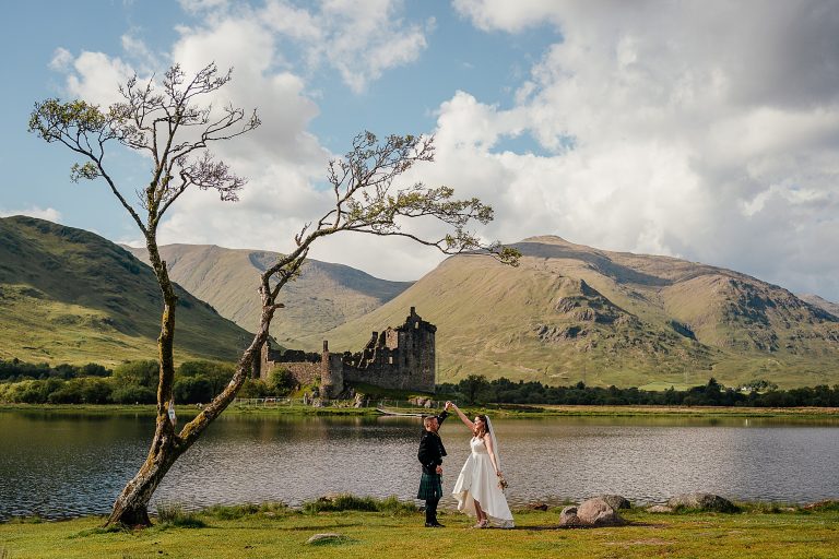 bride and groom dancing in front of a view of kilchurn castle on loch awe during their micro wedding or mini wedding outdoors in scotland
