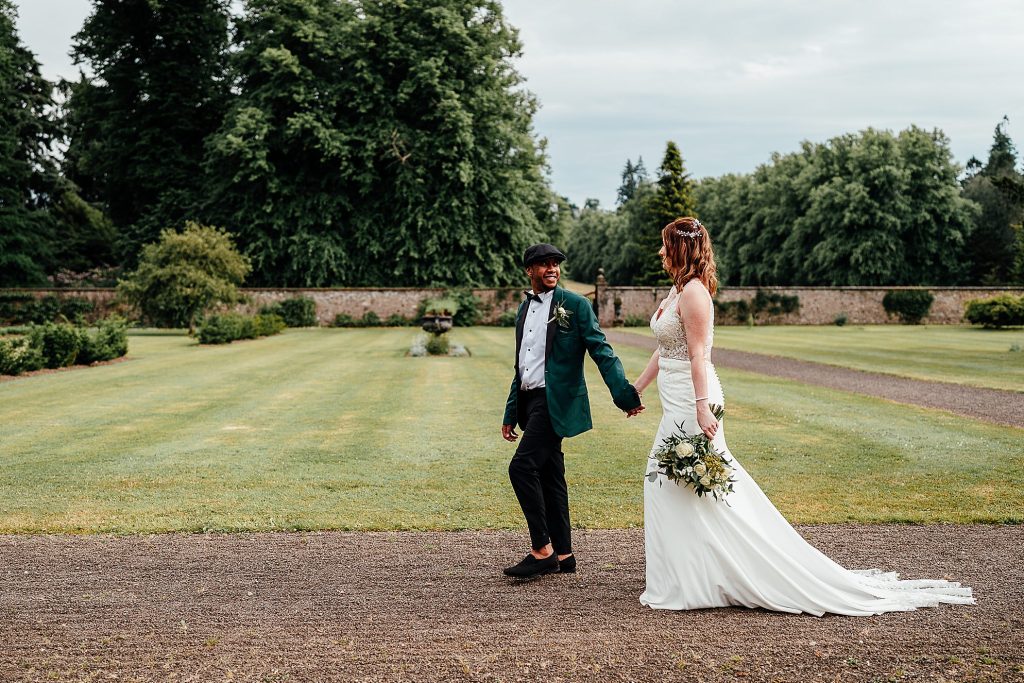 bride and groom walking hand in hand through murthly castle gardens during their outdoor wedding ceremony scotland