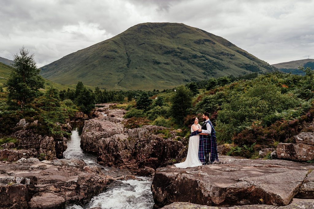 bride and groom standing on rock by a waterfall in glencoe laughing and holding hands by glencoe elopement photographer