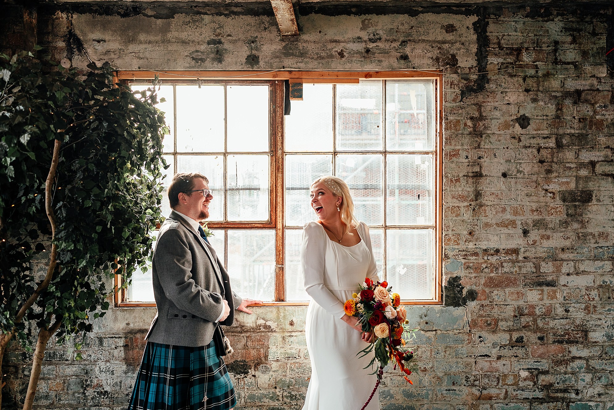 bride and groom pose infront of windows inside the industrial old building of the biscuit factory in leith edinburgh with green and red autumnal tones