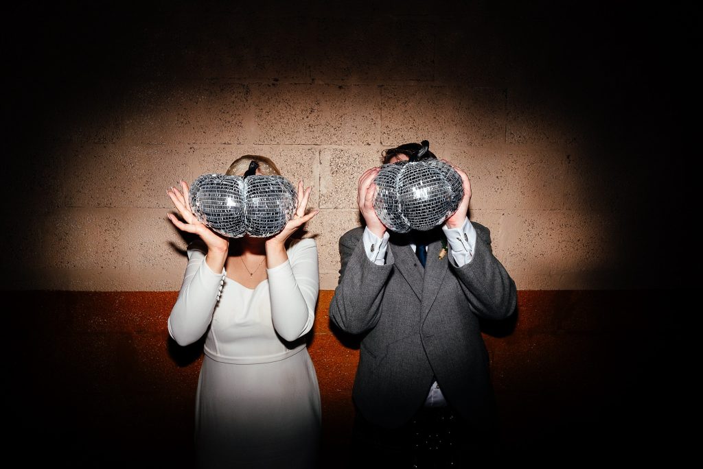bride and groom hide behind disco pumpkins at their wedding reception evening party at the biscuit factory downstairs