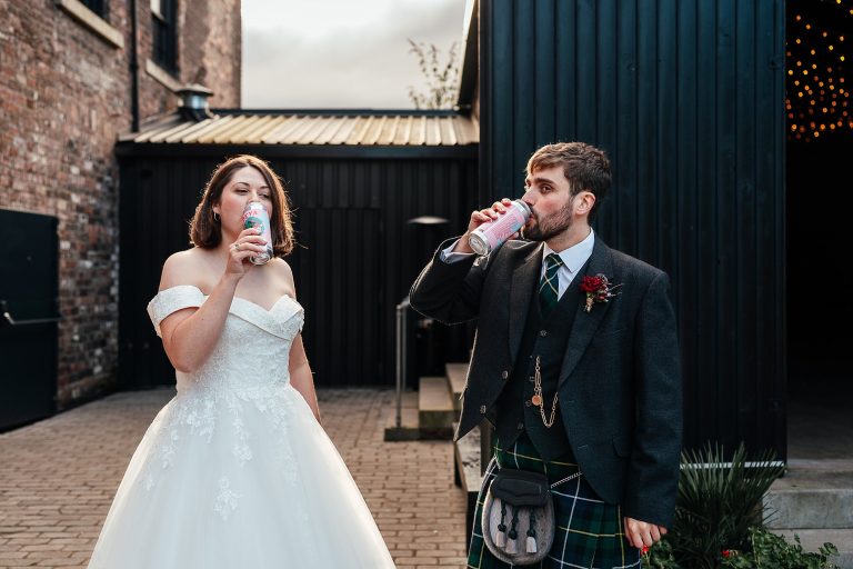 bride groom drink beer from cans outside the outhouse at the engine works in glasgow an old industrial building with red brick walls