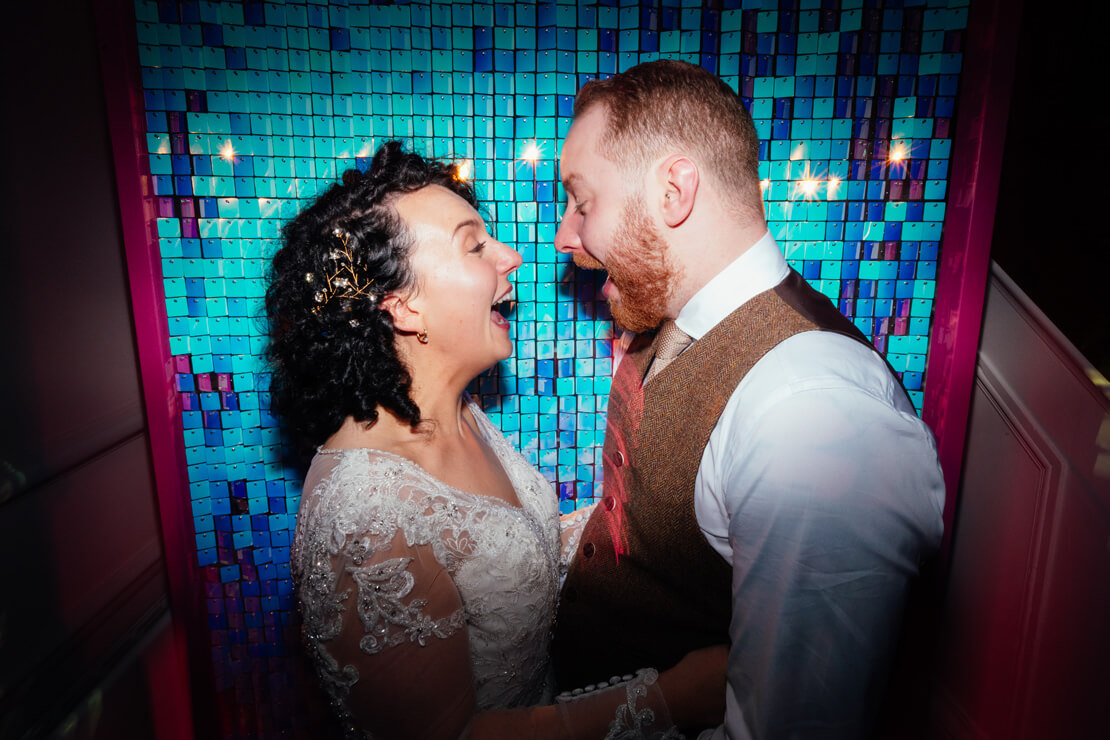bride and groom laugh at each other in front of blue disco backdrop at their wedding